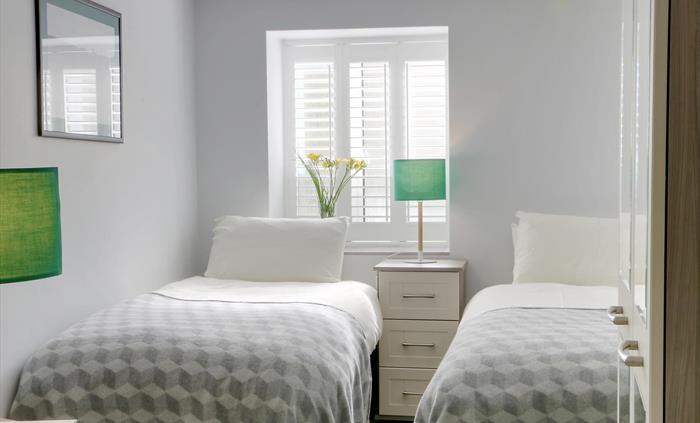 Twin bedroom with soft grey decor, mirrored wardrobe, and geometric bedding, filled with natural light from shuttered windows.
